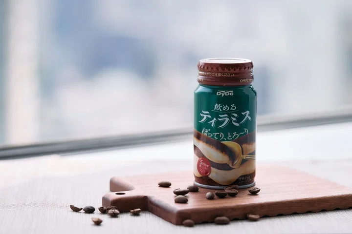 「飲めるティラミス」のボトル缶とコーヒー豆が木製のボード上に置かれている様子