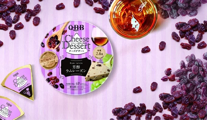 QBBチーズデザート芳醇ラムレーズンのパッケージと周囲に散らしたレーズン、ラム酒のグラス