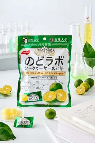 「のどラボ シークヮーサーのど飴」のパッケージとシークヮーサーの実、試験器具