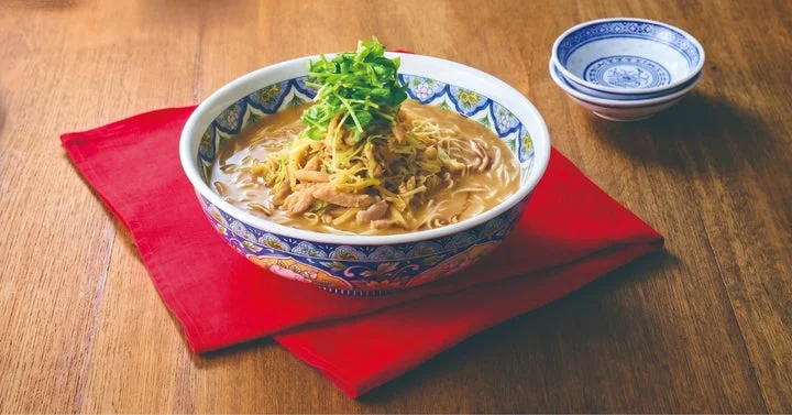黒酢鶏白湯麺の一杯。麺の上に野菜が盛られ、小皿が添えられている。