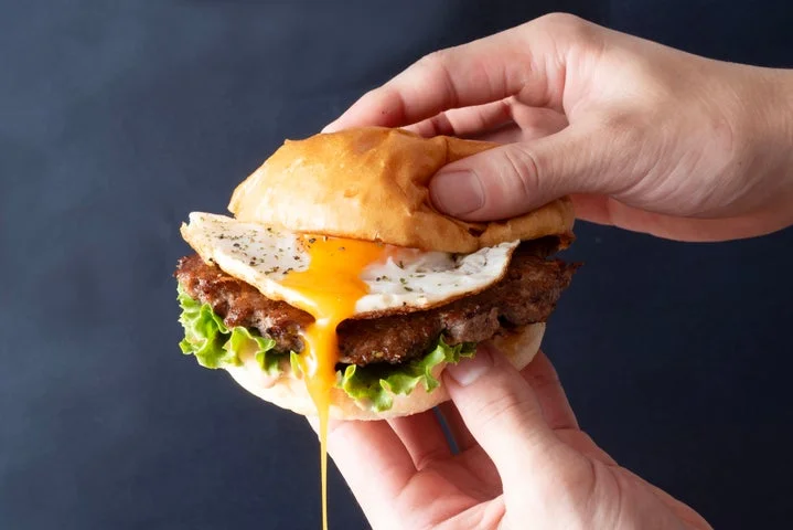 手に持ったハンバーガーから、半熟の黄身がとろりと流れる様子。