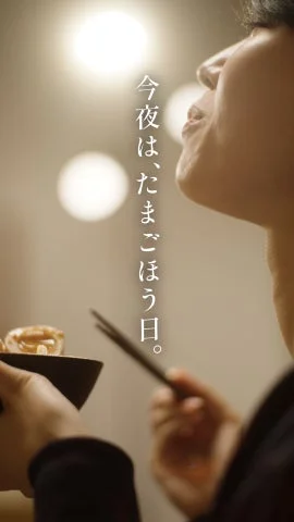 「今夜は、たまごほう日。」というメッセージと共に、夜にたまごを食べる人物の横顔