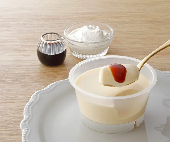 スプーンですくったプリンにカラメルソースがかかっている様子と、生クリーム、ソース容器