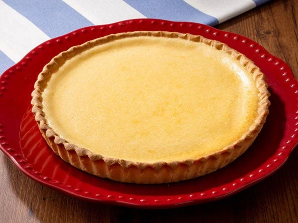 赤い皿に乗ったホールサイズのチーズタルト。表面は黄金色に焼き上がっている。