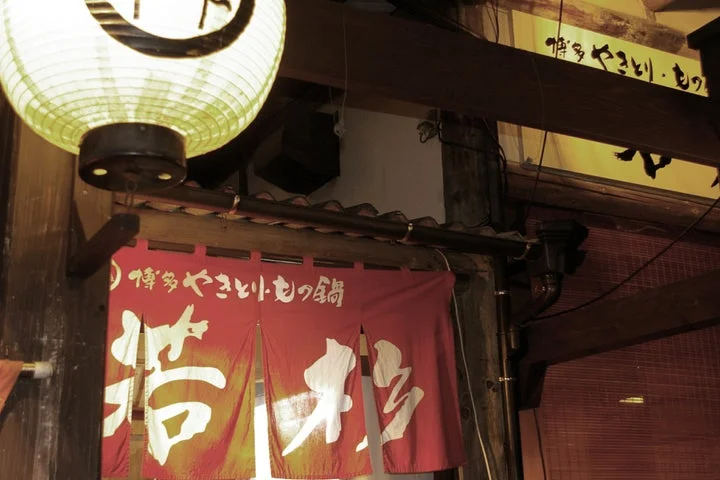 「博多やきとり・もつ鍋」と書かれた赤い暖簾と提灯が下がる店舗の入り口