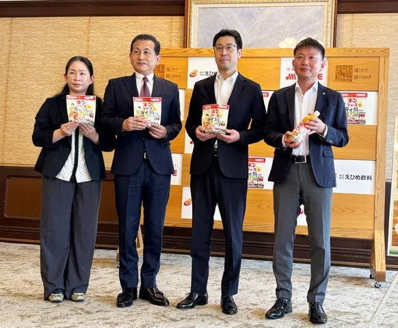愛媛県庁での新商品発表・試食会に出席した関係者4名が商品を持って並ぶ様子。