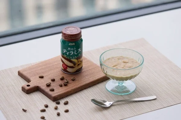 「飲めるティラミス」のボトル缶、中身を注いだグラス、スプーン、コーヒー豆