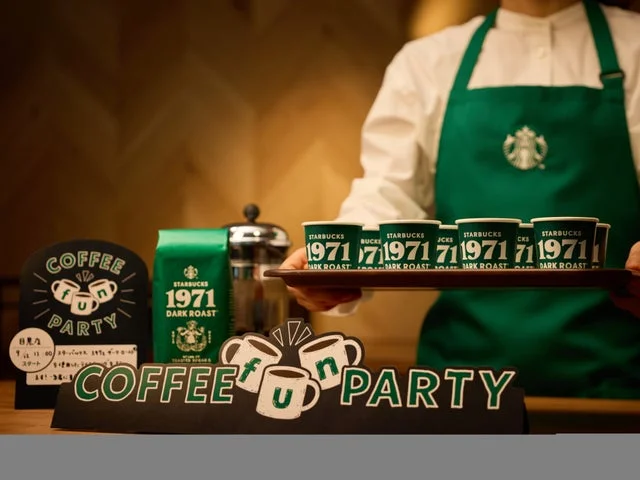 COFFEE fun PARTYと書かれたボードと、1971 ダーク ローストの試飲用カップを持つパ