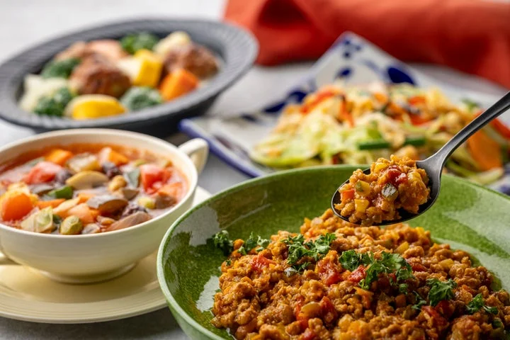スプーンですくったキーマカレーと、スープや炒め物などの料理が並ぶ食卓