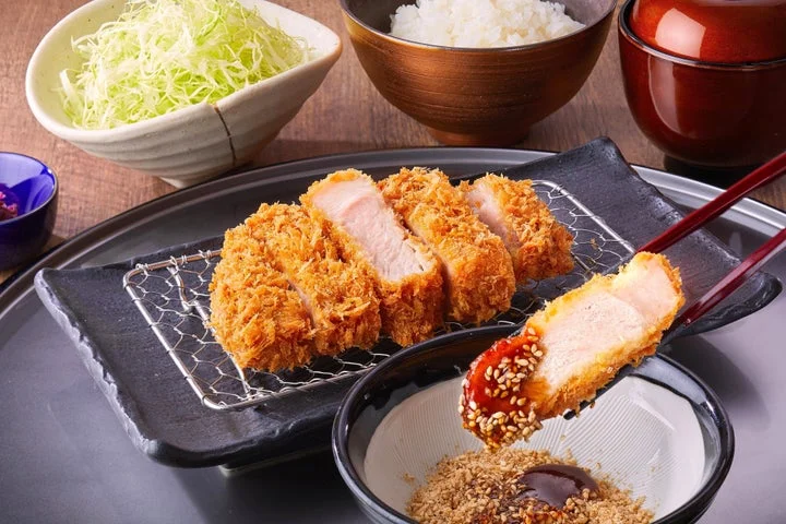 とんかつ定食（かつ、キャベツ、ご飯、味噌汁）を箸で持ち上げている様子