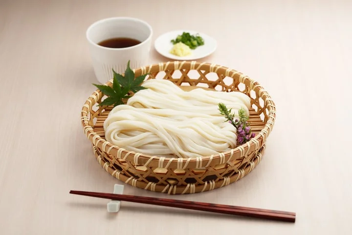 ざるに盛られた茹で上がったうどんと薬味