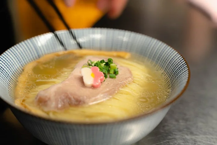 青い縞模様の丼に盛られた鯛塩ラーメン。チャーシュー、ネギ、花の形をしたトッピングが乗っている。