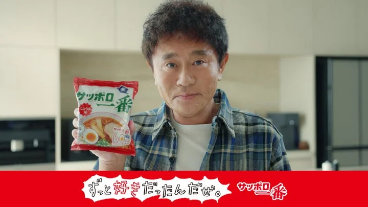 チェック柄シャツの男性がサッポロ一番しょうゆ味のパッケージを手に持ち、下部にCMタイトルとロゴが表示