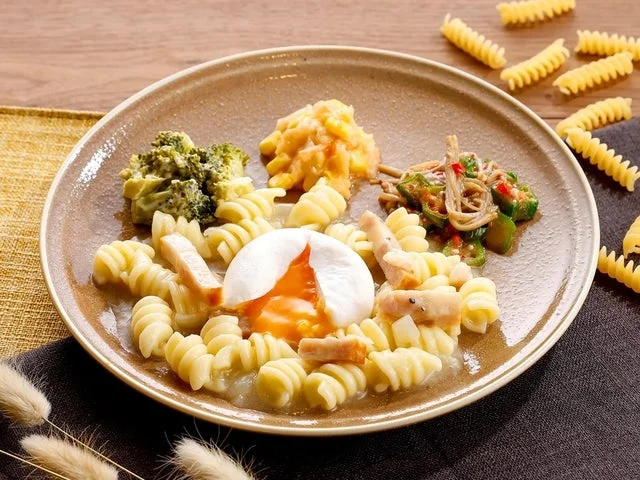 半熟卵をトッピングしたカルボナーラショートパスタと副菜を盛り付けた皿