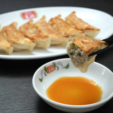 箸で持ち上げられた焼餃子と、皿に並んだ餃子、酢の器