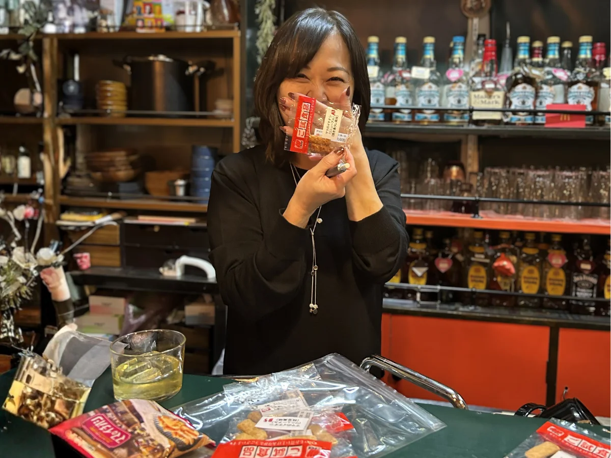 スナック店内で「ママのイチオシ」の小袋を手にする女性