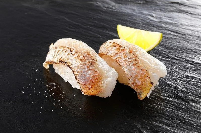 炙りき鯛すだち塩。黒い皿に2貫とすだちが添えられています。