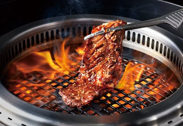 網の上で焼かれている焼肉カルビとトング