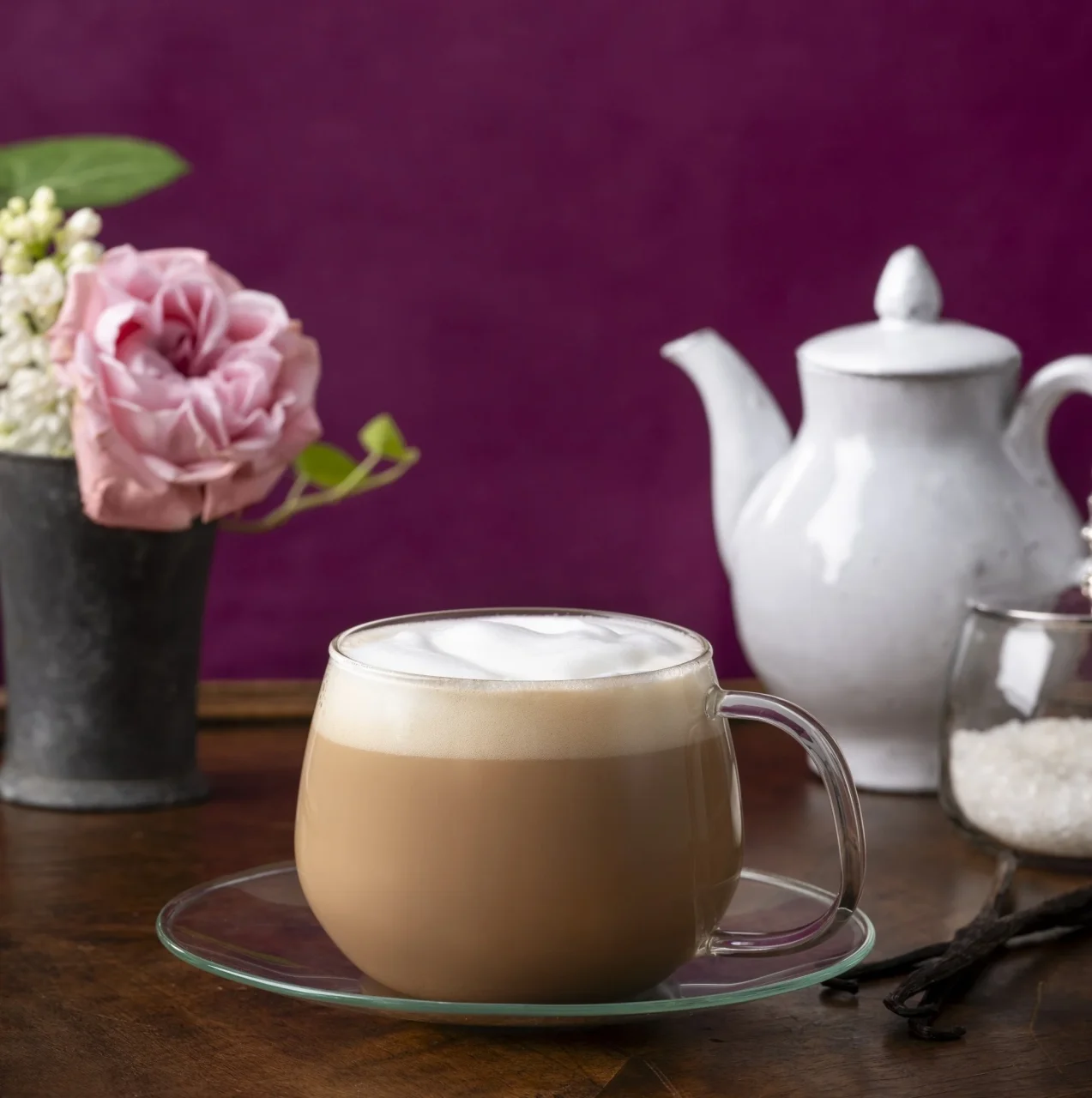 ミルクの泡が乗った紅茶が入った透明なカップとティーポット