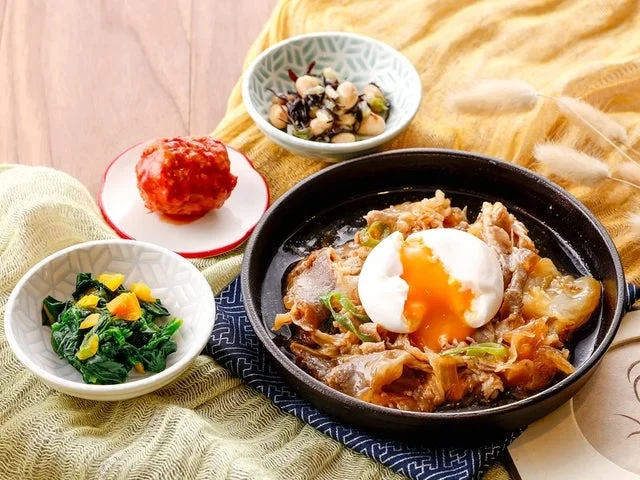 半熟卵をトッピングした牛すき焼きと、肉団子やほうれん草など3種の副菜