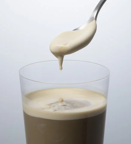 ガラスコップに入ったカフェラテからスプーンでクリームをすくう様子