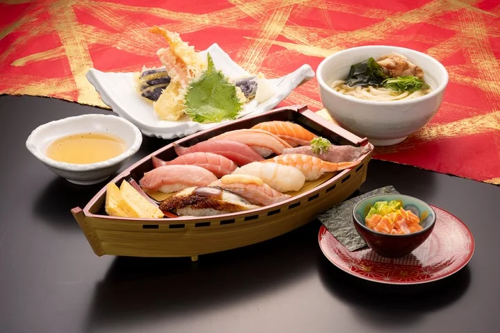 舟形の器に盛られた握り寿司、天ぷら、うどん、小鉢が並んだ食事のセット