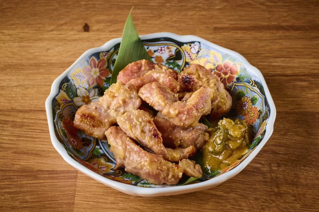 米沢豚の西京焼き。焼き色がついた豚肉と青唐味噌を花柄の皿に盛り付けた様子。