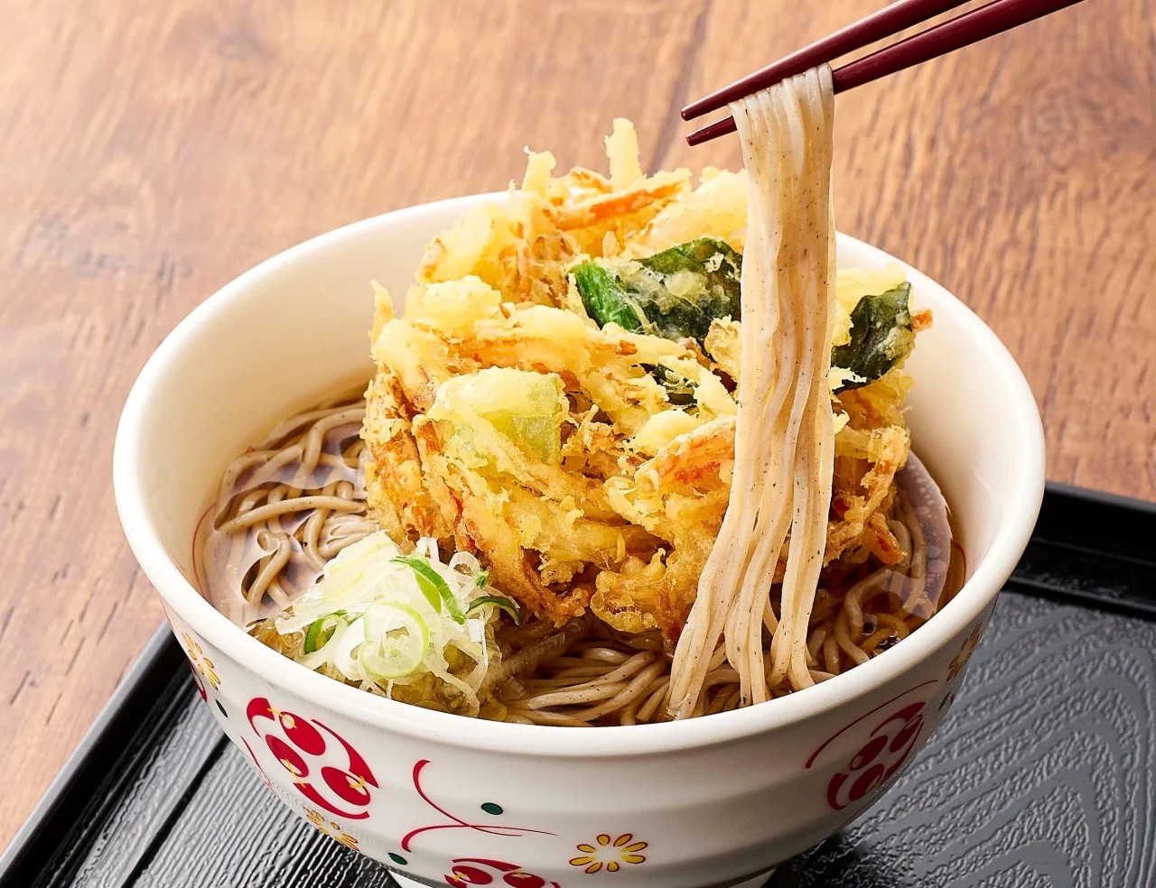 いろり庵きらくのそば丼。かき揚げとネギが乗ったそばを箸で持ち上げている様子。