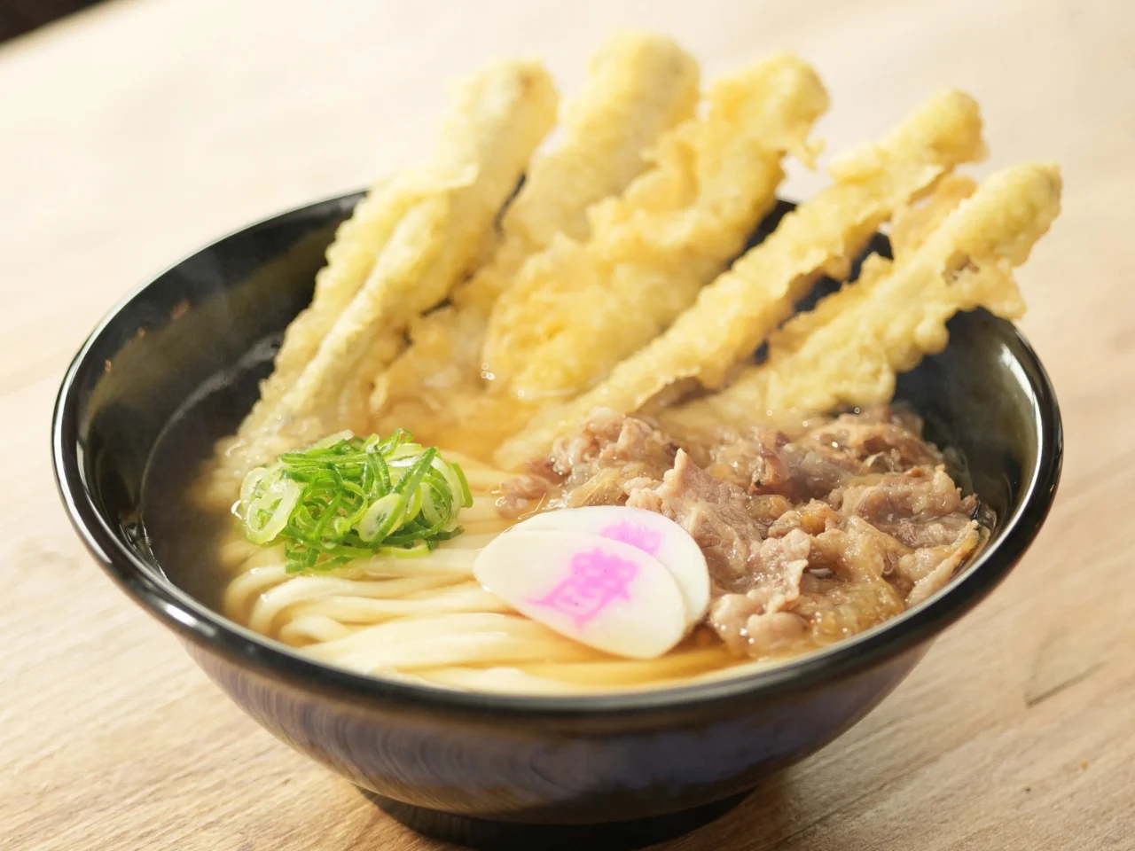 資さんうどんの肉ごぼ天うどん。黒い丼にうどん、肉、ごぼう天ぷら、ネギ、卵が乗っている。