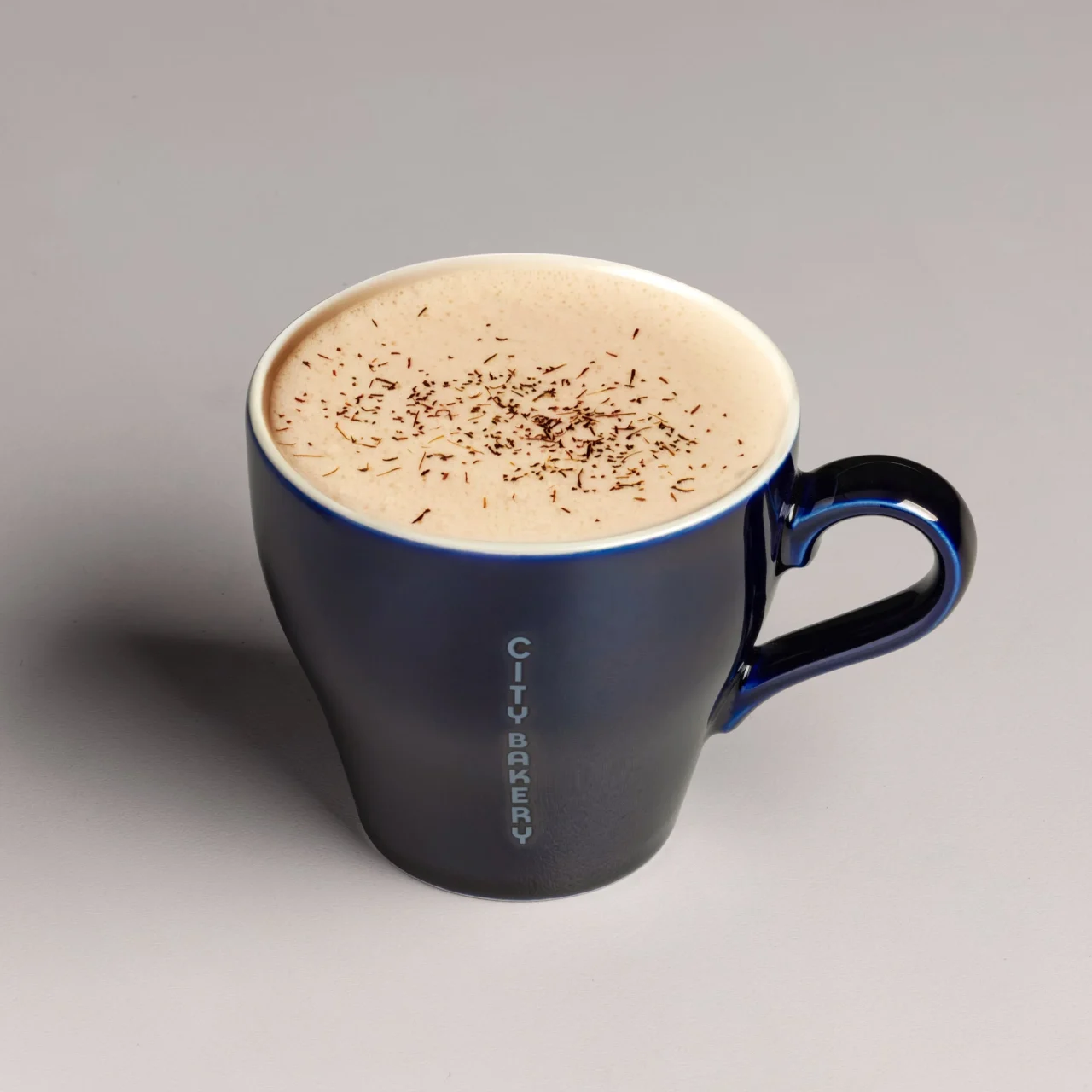 THE CITY BAKERYのアップル烏龍 ティーラテ。青いマグカップに注がれた飲み物で、表面に泡と細かなトッピングが見える。