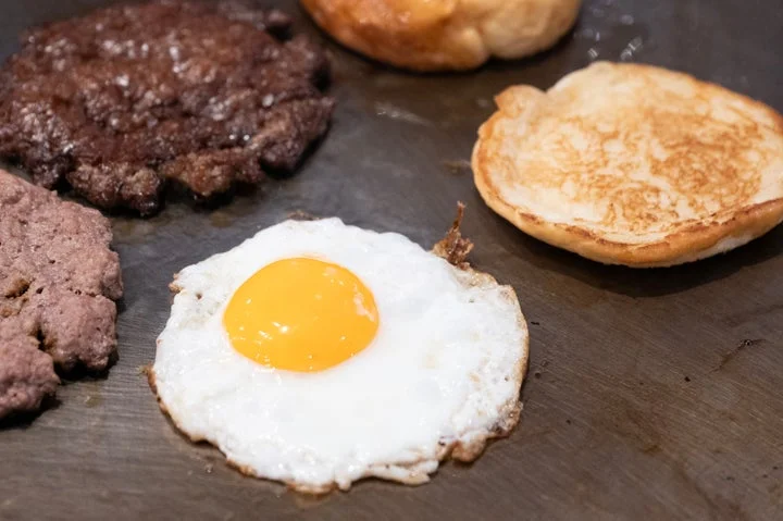 グリドルで焼かれている目玉焼き、パティ、バンズの様子。