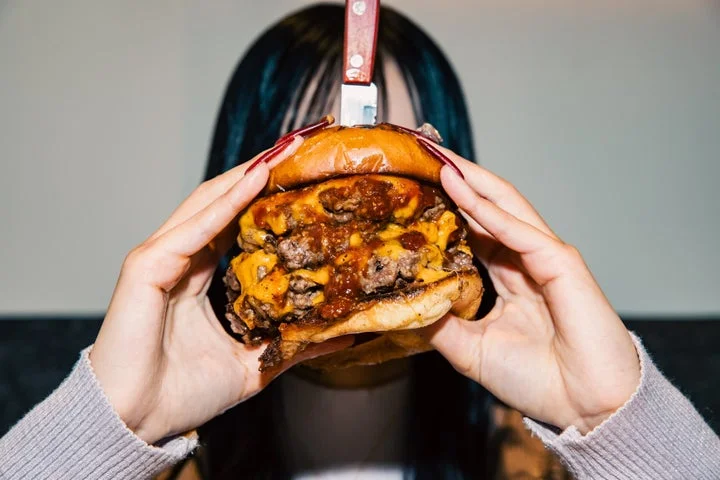 ナイフが刺さったダブルパティのハンバーガーを持つ手