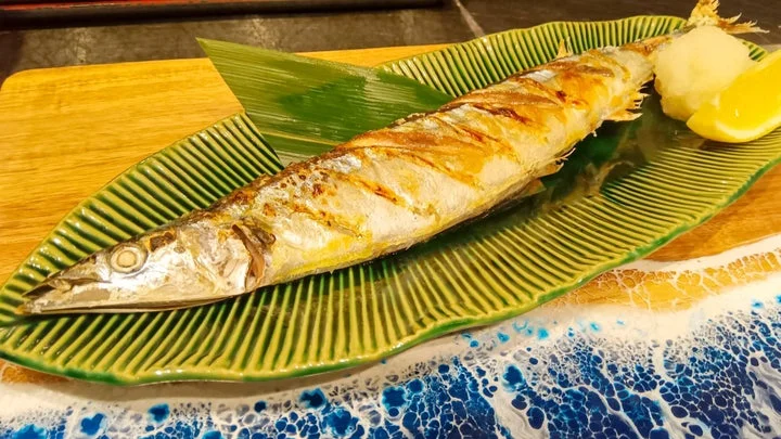 緑の葉の上に盛り付けられた、焼き上がった生さんまの塩焼き。大根おろしとレモン添え。