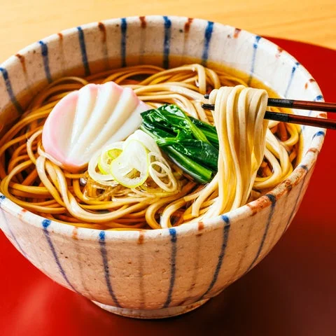 箸で持ち上げられた年越しそば。具材に蒲鉾や小松菜が添えられている