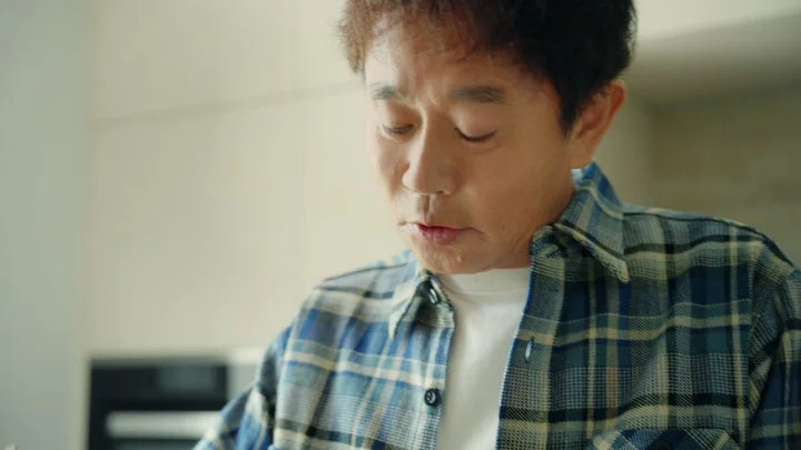 チェック柄シャツを着た男性が目を閉じて麺をすすっている