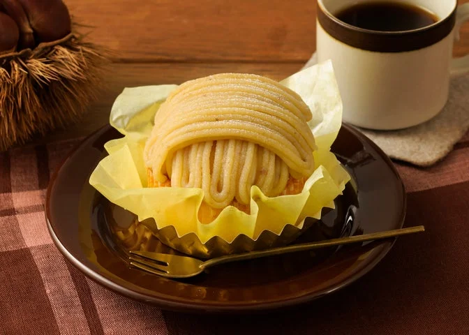 茶色い皿に盛られたモンブランと、背景に置かれた栗とコーヒーカップ