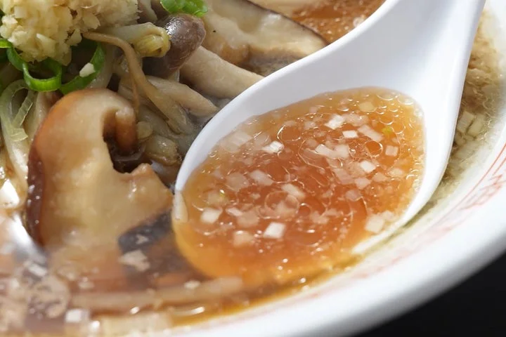 スープをすくったレンゲと、椎茸やしめじ、刻み生姜が浮かぶラーメン