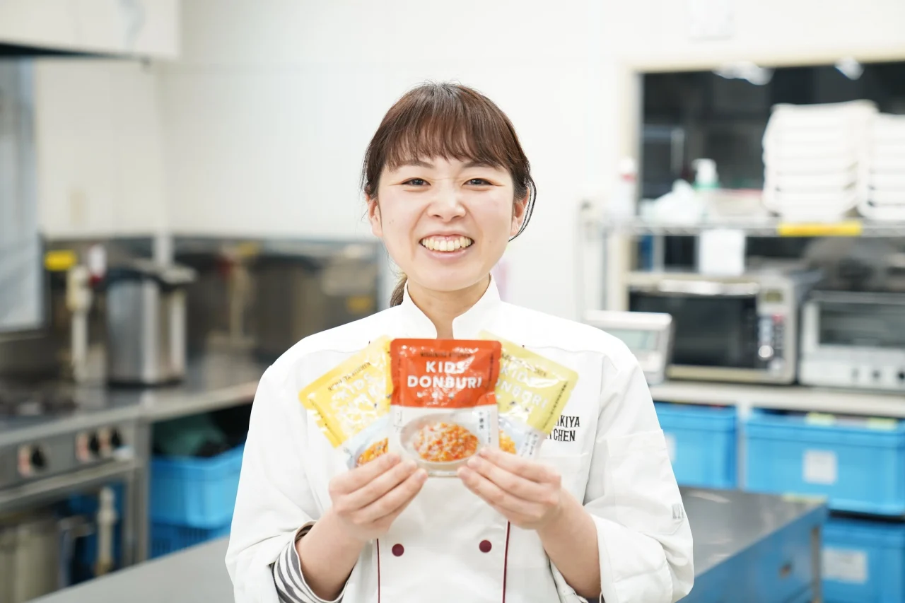 白衣の女性がニシキヤキッチンキッズシリーズのレトルトパック3点を手に持った姿