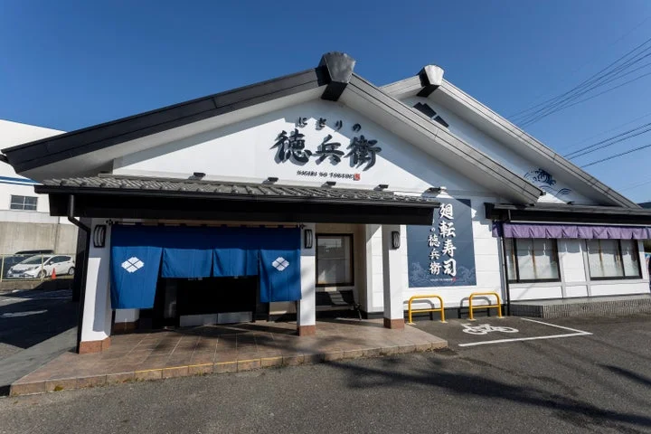 にぎりの徳兵衛の店舗外観。白い壁と青い暖簾が特徴的な和風の建物。
