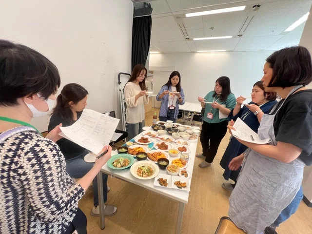 複数の社員がテーブルの上の料理を試食している様子