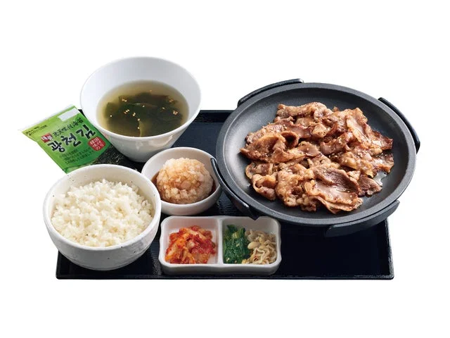 鉄板に焼いたカルビ肉、ご飯、スープ、大根おろし、キムチなどのおかずが並んだセットメニュー