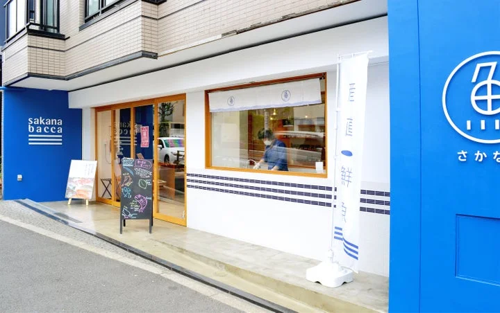 青い外壁にロゴと店名が施された鮮魚専門店サカナバッカの店舗外観