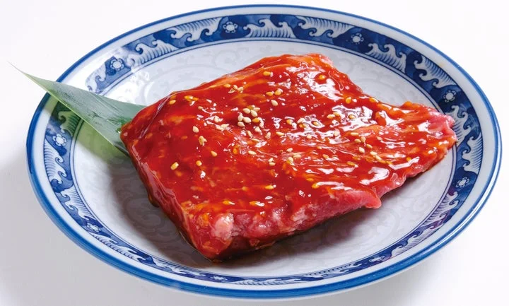 赤いタレとごまをかけた厚切りの生肉が青白磁の皿に盛られている