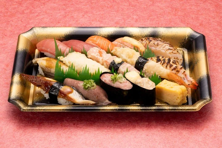 黒金模様の長方形の器に、炙りや天ぷらなど加熱したネタの握り寿司が並んだ様子