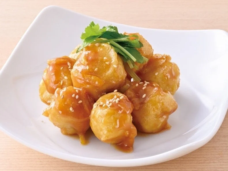 里芋のゆず味噌ポテト。白い皿に盛られた揚げ物にソースと白ごま、香菜が添えられている