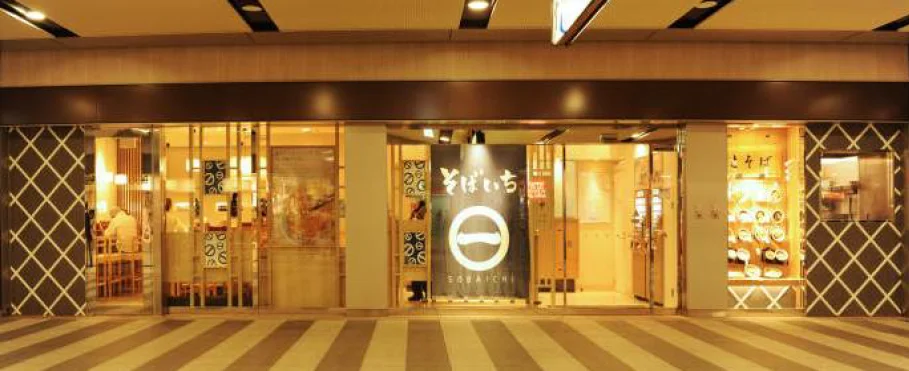 そばいちの店舗外観。暖色系照明の店内と看板が確認できる。