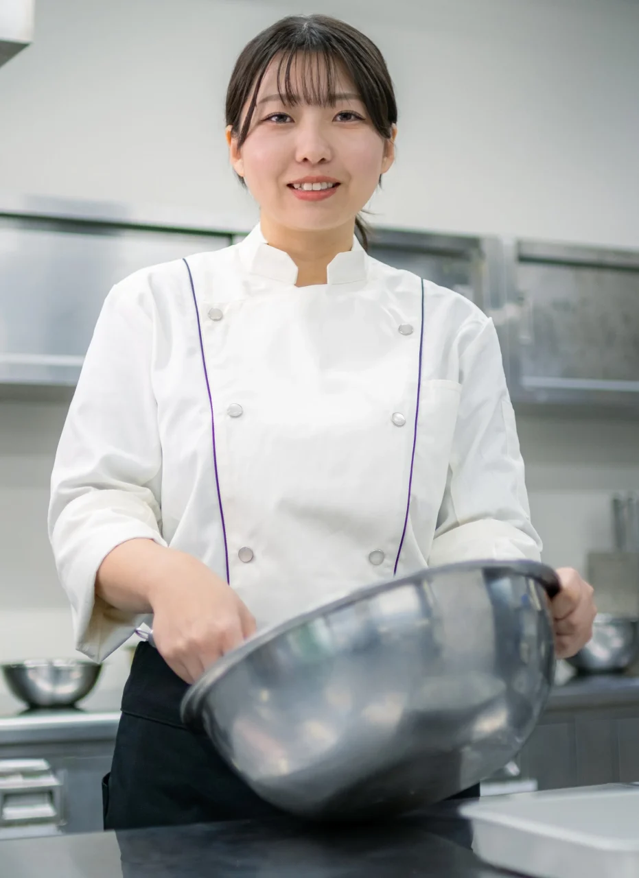佐藤真衣子。白いシェフコートを着て、ステンレスボウルを持つ女性パティシエ