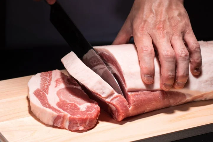 包丁で豚肉の塊をカットしている調理風景