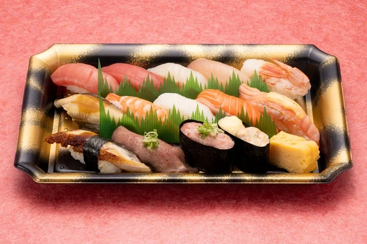 黒と金の長方形の器に、サーモンやまぐろ、炙りネタなど多種多様な握り寿司が並べられている