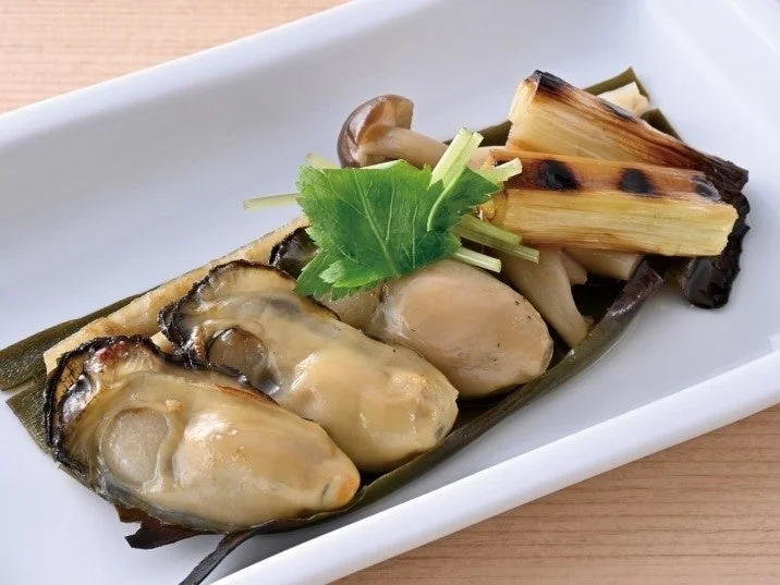 牡蠣ときのこの昆布焼。牡蠣とキノコを昆布で巻いて焼き、葉物で飾った料理
